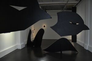 Au premier plan, deux grandes têtes d'oiseau noires sont suspendues dans la salle 3. Au sol, une vague de carton et une autre forme noire composent le décor d'Automne, le grand théâtre, une oeuvre de Raphaël Larre.