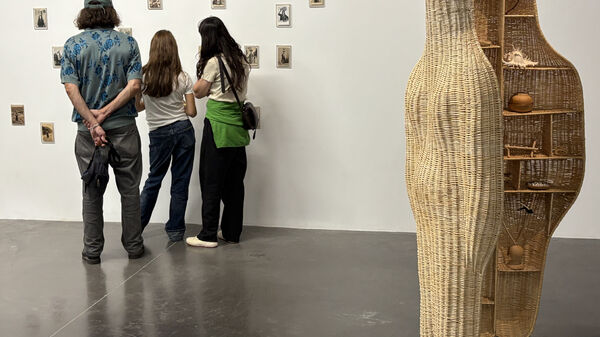 Une silhouette de femme en osier tressé regarde trois personnes scrutant une série de cartes postales anciennes de femmes portant sur leurs têtes des contenants au contenu secret.